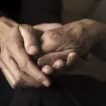A younger person gently holding the hand of an older person, showing support and care. The image focuses on their hands, highlighting the contrast in age, warmth of human connection, and visible signs of Dupuytren’s contracture symptoms.