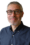 A middle-aged man with short gray hair, glasses, and a trimmed beard, wearing a navy blue button-up shirt, smiles at the camera—portraying optimism often seen in those seeking Dupuytrens contracture treatment UK.
