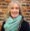 A smiling woman with long gray hair, wearing a light blue scarf and dark sweater, stands in front of a brick wall holding a clarinet—her joy undimmed despite living with Dupuytren’s contracture symptoms.