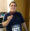 A smiling man wearing a dark sports shirt and a race bib holds up a medal in a kitchen, celebrating his achievement despite recently managing Dupuytren’s contracture symptoms.