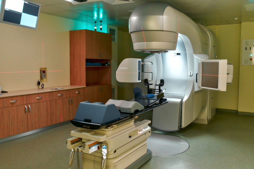 A modern hospital room with a large linear accelerator used for radiation therapy, featuring a treatment bed and equipment under bright overhead lighting—ideal for patients with conditions like Dupuytren’s contracture symptoms or Ledderhose disease.