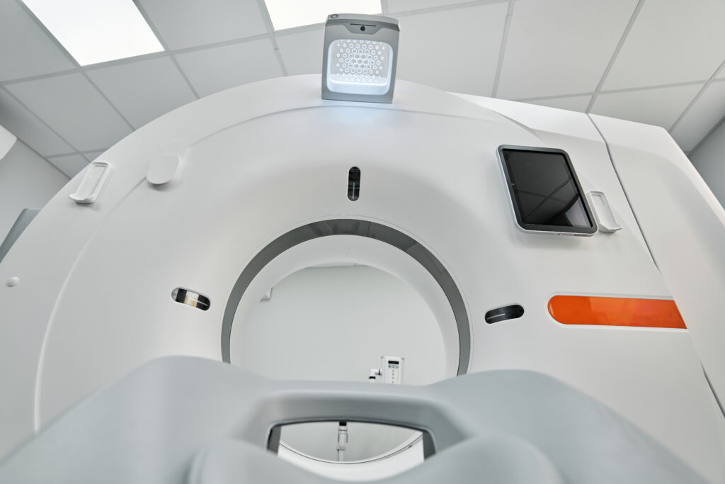 Close-up view of a modern medical CT scanner from the patient’s perspective, highlighting features used in diagnosing conditions such as Dupuytren’s contracture disease, with a clear view of the circular opening and control panel in a bright exam room.