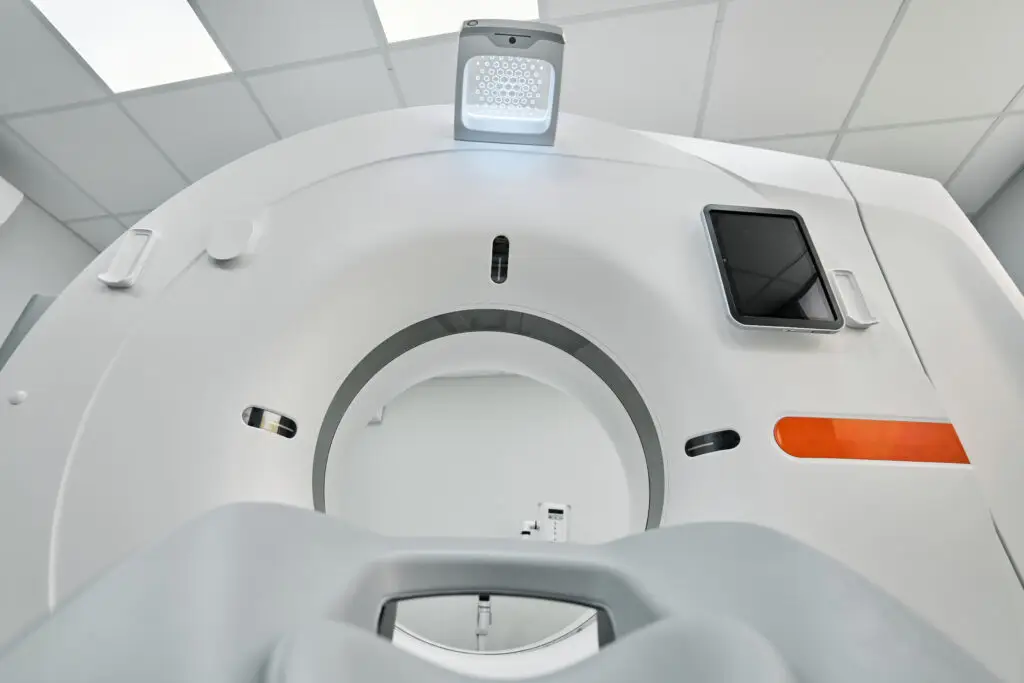 Close-up view of a modern medical CT scanner from the patient’s perspective, highlighting features used in diagnosing conditions such as Dupuytren’s contracture disease, with a clear view of the circular opening and control panel in a bright exam room.