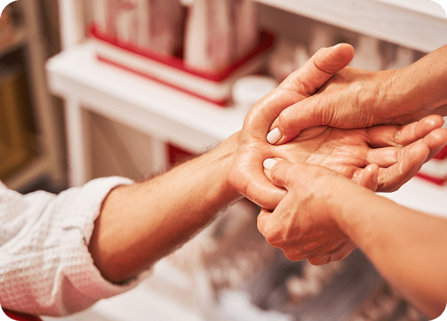 Close-up of one person gently massaging another’s palm with both hands, suggesting a hand therapy or relaxation treatment in a clinical or wellness setting, possibly as part of Dupuytrens contracture treatment UK.