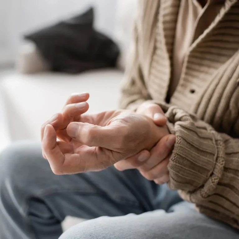 partial view of senior man with parkinsonism holding trembling hand while sitting at home